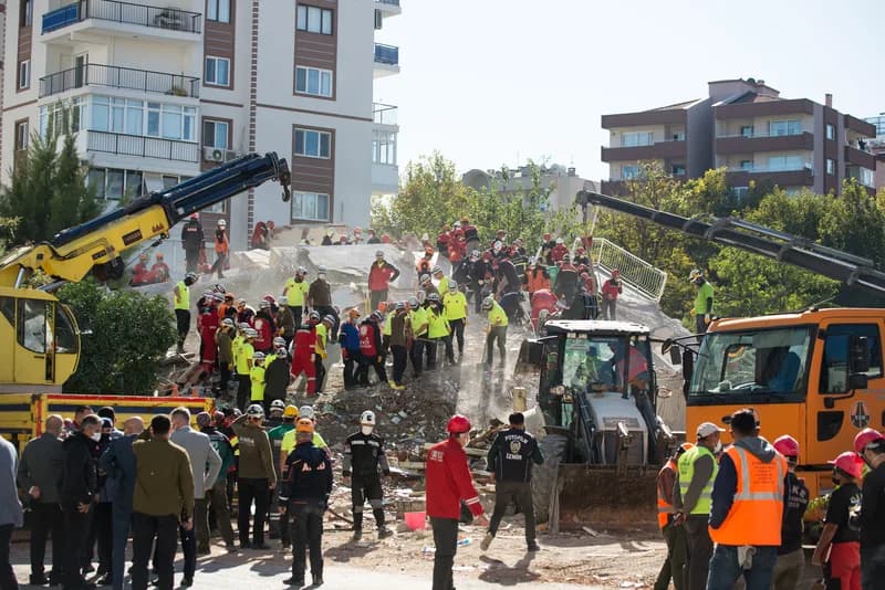 Rescue workers and volunteers clearing concrete debris from a collapsed multi-storey building, with excavators working alongside them.