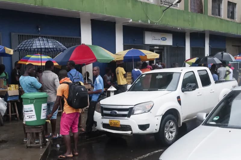 People queue in a street beside a bucket of chlorinated water set out for handwashing during an Ebola outbreak.