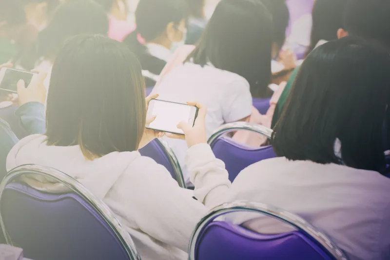 A student at a desk looking down at a smartphone.